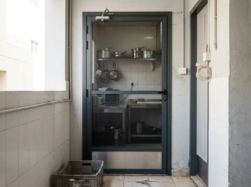 Hinged mosquito screen door with a closer and kick plate at the kitchen entrance of a café