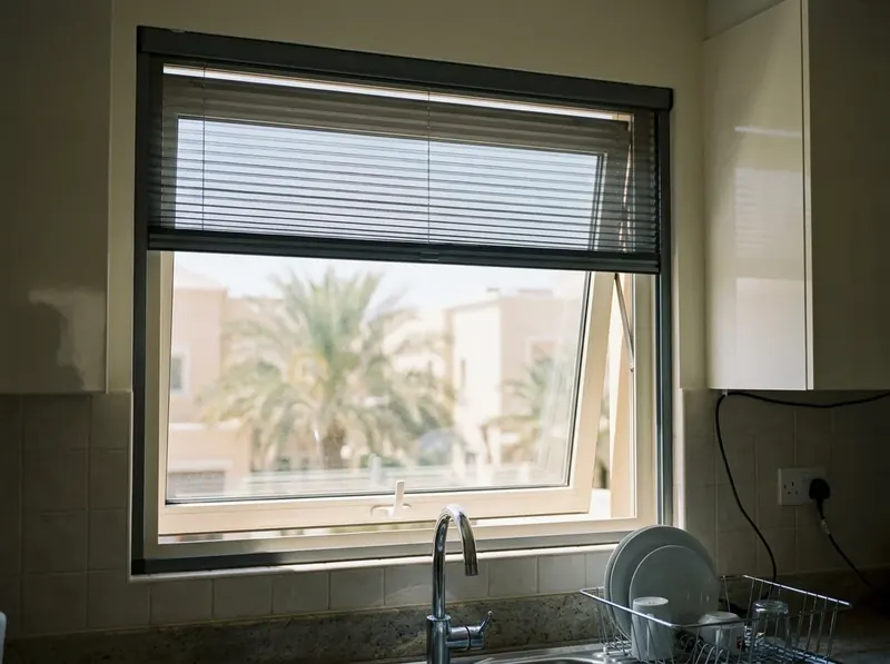 Vertica pleated mosquito screen pulled down over a small kitchen window above the sink, horizontal folds