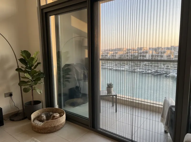 Pleated mosquito screen on the canal-facing terrace door of an Al Raha Beach townhouse, marina boats beyond