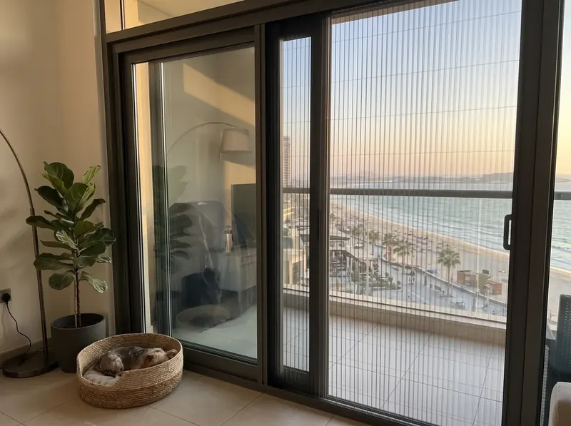 Pleated mosquito screen on a JBR balcony door, the beach and The Walk below