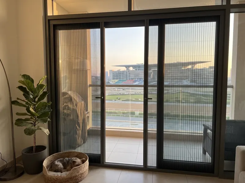 Pleated mosquito screens on the terrace door of a Meydan townhouse, the racecourse grandstand in the distance