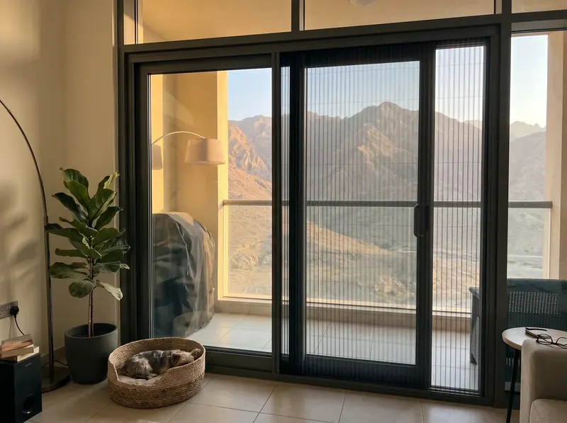 Pleated mosquito screens on the sliding doors of an Al Hamra villa, Hajar mountains behind