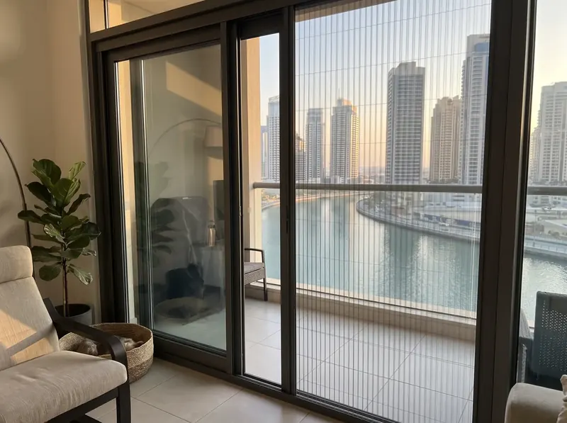 Pleated mosquito screen on the balcony door of an Al Majaz tower flat, the lagoon below