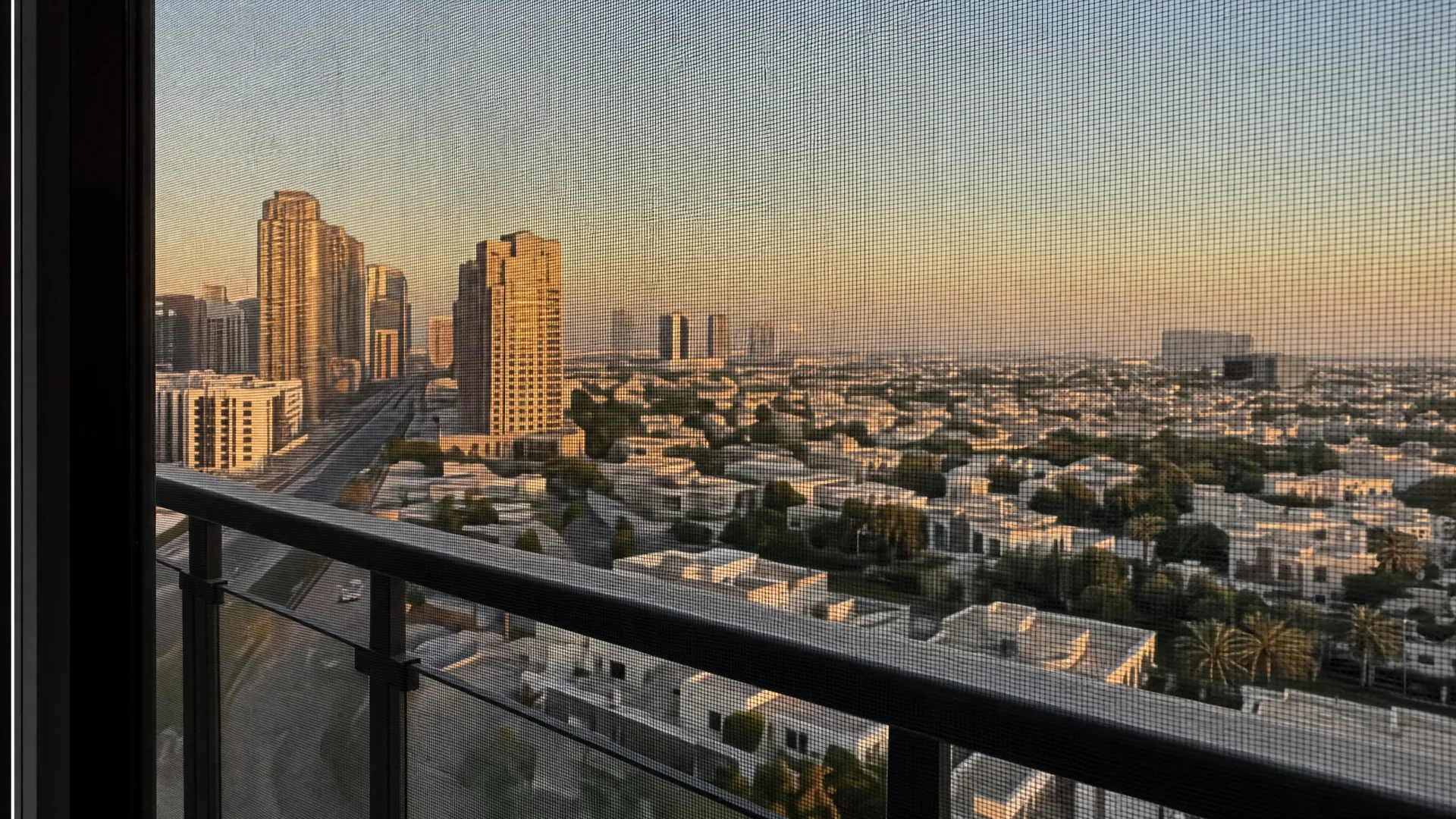 A UAE panorama of residential towers and low-rise districts, an insect screen on the window in front